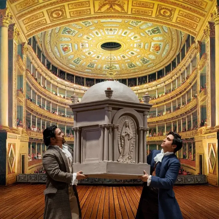 Dos hombres con trajes históricos se encuentran en el escenario de un teatro, sosteniendo una gran maqueta ornamentada de un edificio abovedado. Al fondo se ve un auditorio profusamente decorado, lleno de público sentado.